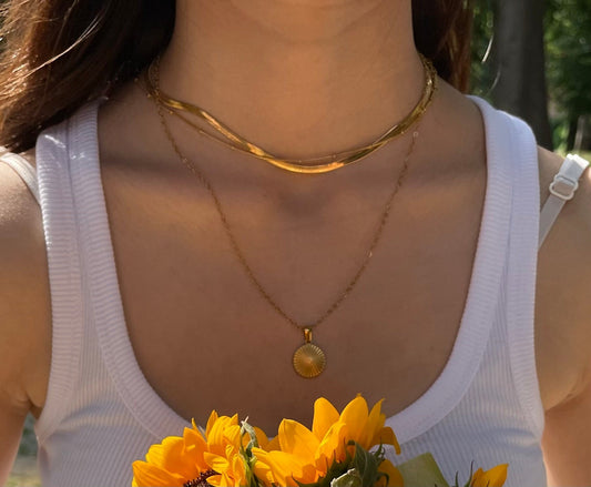Drei goldene Ketten im Layering-Stil auf weißem Oberteil kombiniert.