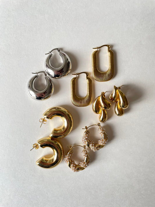 Woman wearing minimalist gold necklace and small hoops in a casual white blouse.
